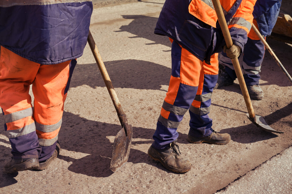 Straßenarbeiter in Uniform erneuern mit Schaufeln den Asphalt